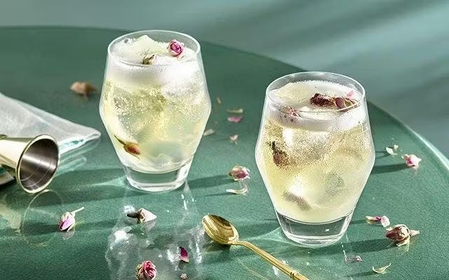 Two light sparkling cocktails in rocks glasses with floral garnish
