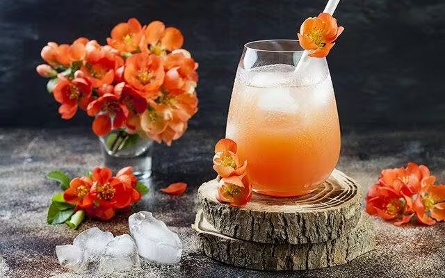 Orange cocktail in a tumbler with floral garnish