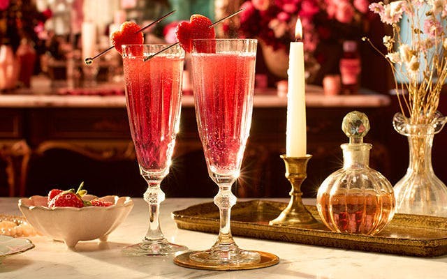 Two sparkling pink cocktails in champagne flutes with strawberry heart garnish