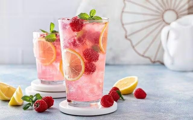 Pink sparkling cocktail in highball glass with raspberry and mint garnish