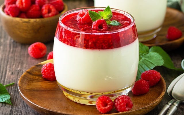 Vanilla panna cotta is topped with raspberry gin and pomegranate jelly and garnished with fresh raspberries and mint