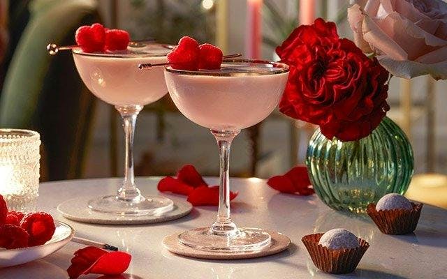 Two creamy pink cocktails in coupe glasses with raspberry heart garnishes