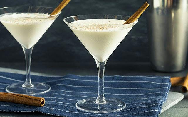 Two creamy white cocktails in martini glasses garnished with cinnamon sticks