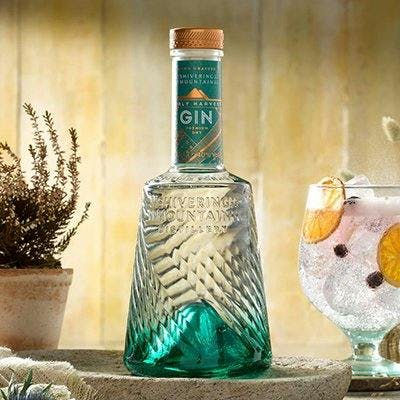 A bottle of shivering mountain gin next to a G&T with ice and orange slices