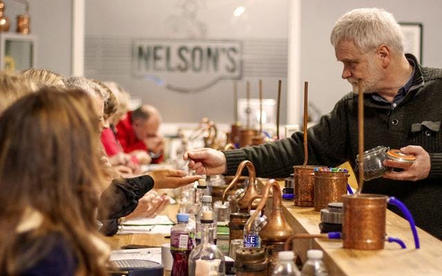 A man assists a group learning how to make their own gin at work benches