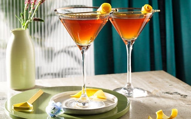 Two dark cocktails in martini glasses with lemon peel garnish