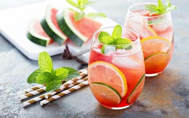 A refreshing watermelon gin and tonic, garnished with a sprig of mint and a few slices of lemon and lime