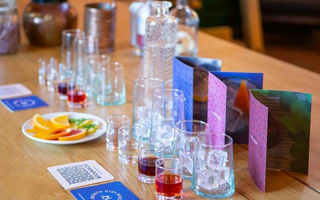 Tasting glasses, fruit and samples of gin are laid out on a table.
