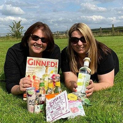 Two friends sitting on the glass with all the goodies from August's Gin of the Month box layed out in front of them