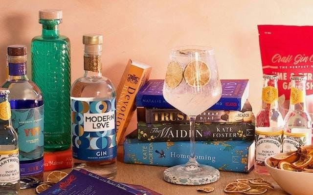 A collection of books, a gin and tonic in a glass and bottles of gin and tonics surrounding