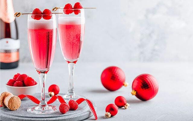 Two pink sparkling cocktails in champagne flutes with raspberry garnish