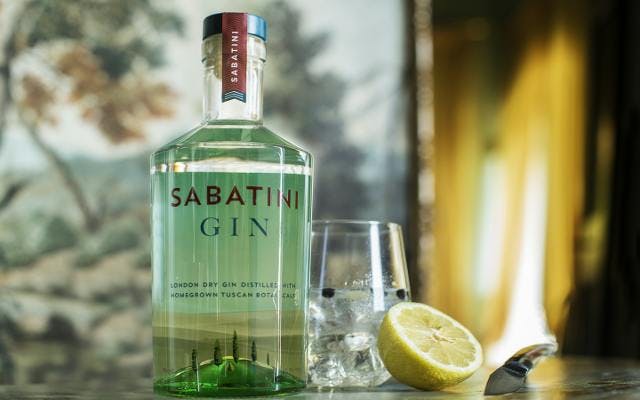 Sabatini gin bottle and lemon next to a g&T