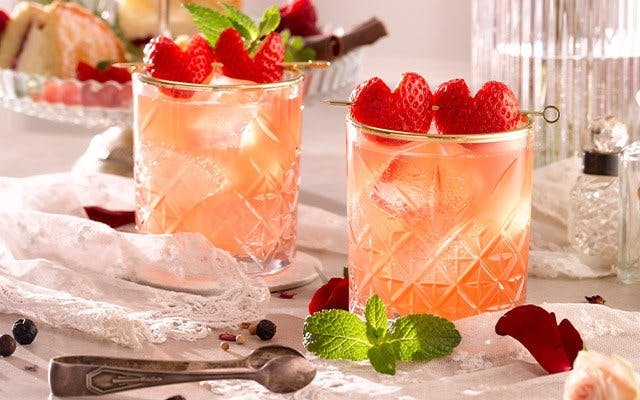 Two light pink sparkling cocktails in rocks glasses with strawberry heart garnishes