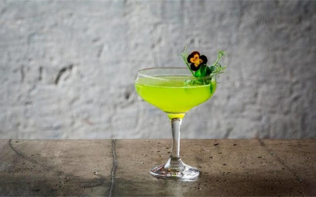 Peas and mint bright green cocktail in martini glass with gin and edible flowers to garnish