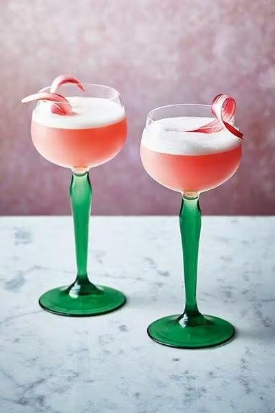 Two pink cocktails in coupe glasses with rhubarb ribbon garnish