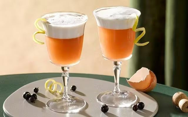Two foamy orange cocktails in wine glasses with lemon twist garnish