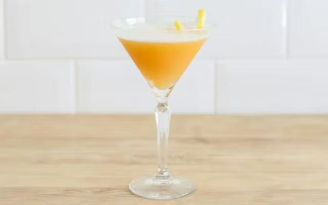 Yellow cocktail in a Martini glass with lemon peel garnish