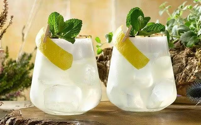 Two light sparkling cocktails in rocks glasses with mint and lemon peel garnish