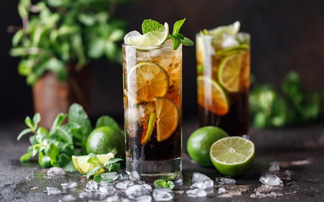 Dark cocktail in a highball glass filled with ice, fresh lime and topped with mint