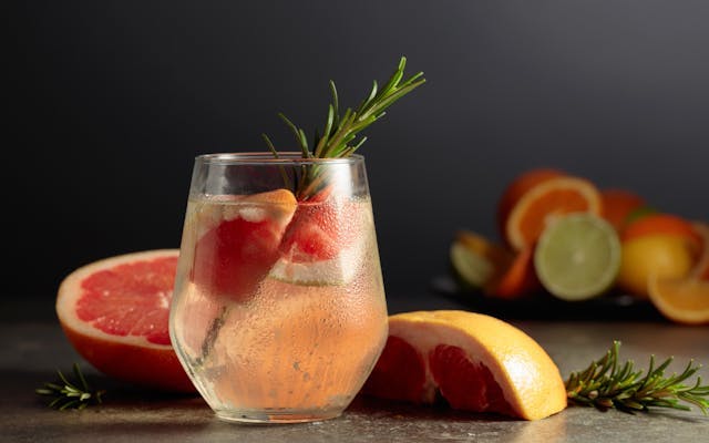 Light pink cocktail in a tumbler garnished with a grapefruit slice and rosemary sprig