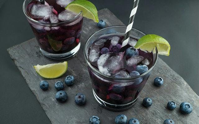 Homemade blueberry gin with blueberries, ice and lime