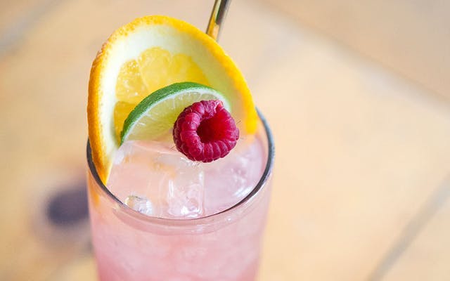 Pink florodora cocktail over ice garnished with lemon lime and raspberry