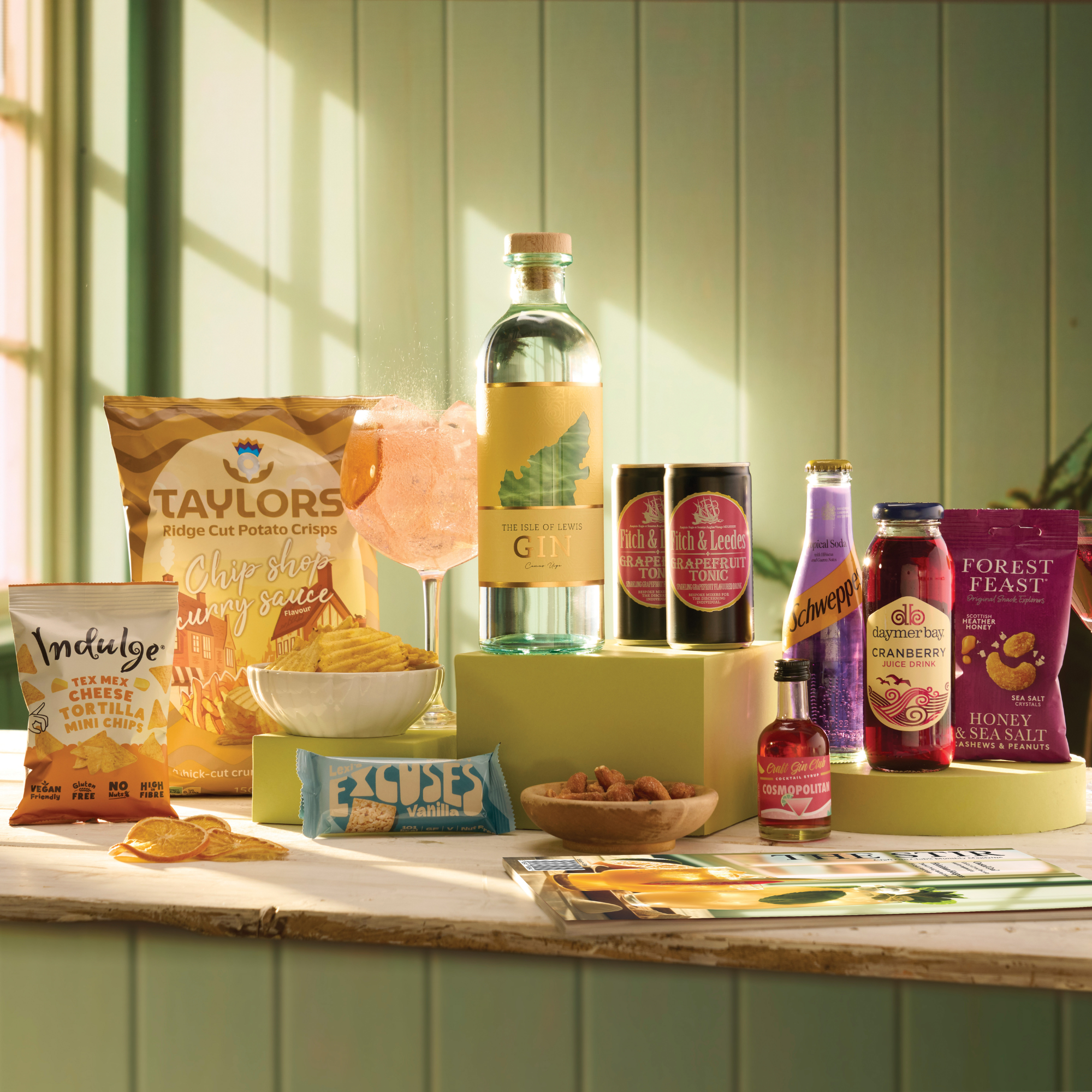 Table with snacks, drinks, and a magazine against a green paneled wall.